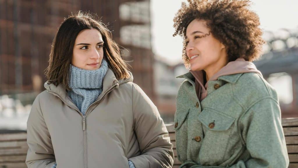 A two women talking outdoors in winter coats.