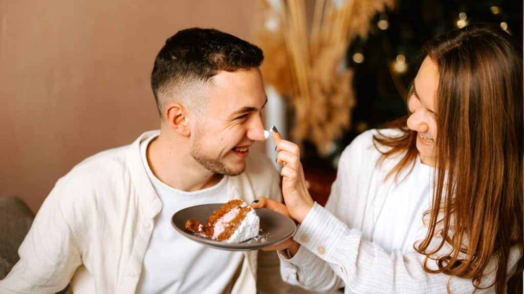 A woman applying cream of a cake on her husband’s nose.