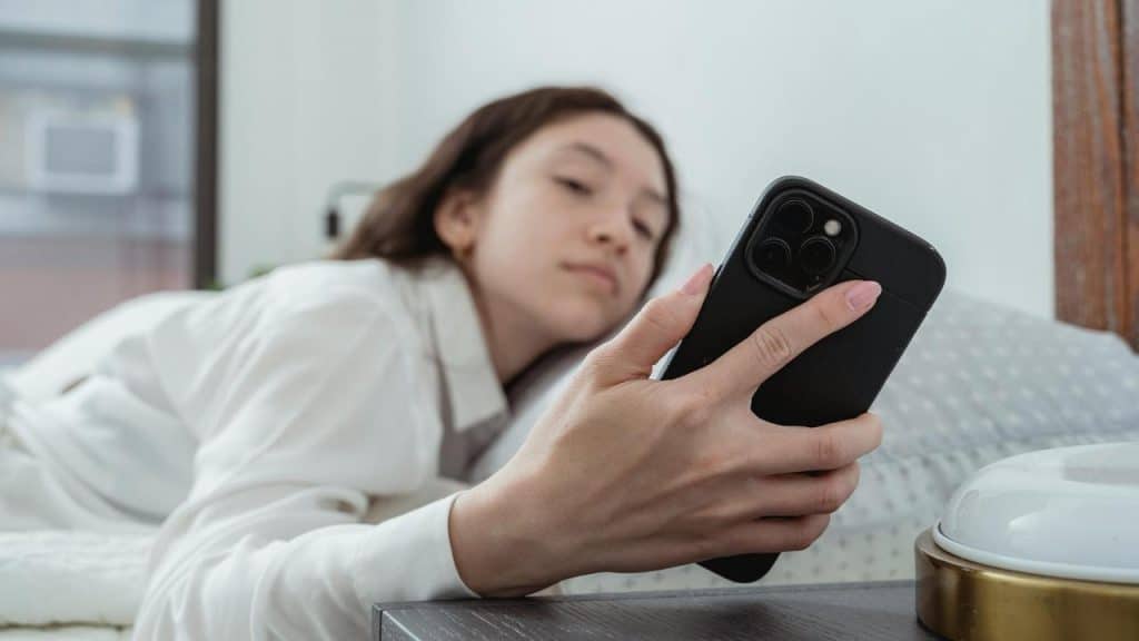 A woman lying in bed looking at her phone.