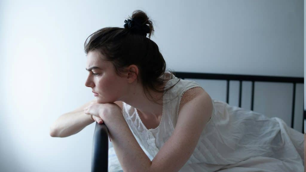 An upset woman resting her head on her hands which are placed on the edge of a couch.
