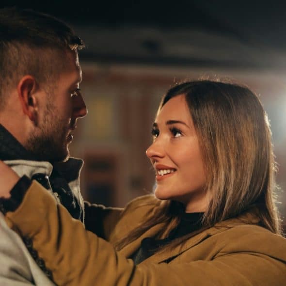 A beautiful couple looking in each other's eyes while standing close outdoors at night.