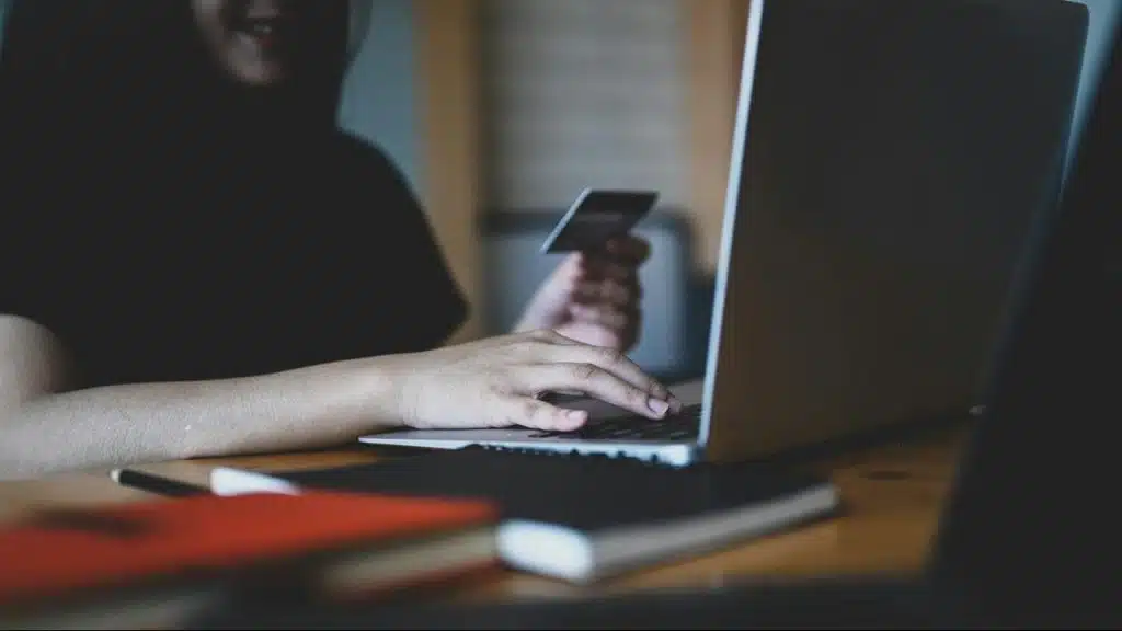 A person using a laptop while holding a credit card.