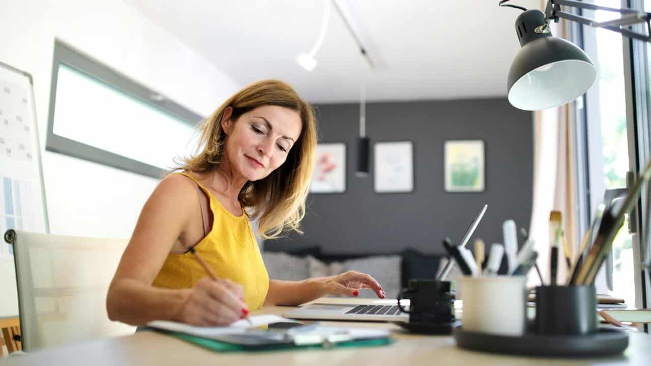 A woman writing something on a paper while performing calculations on a calculator.