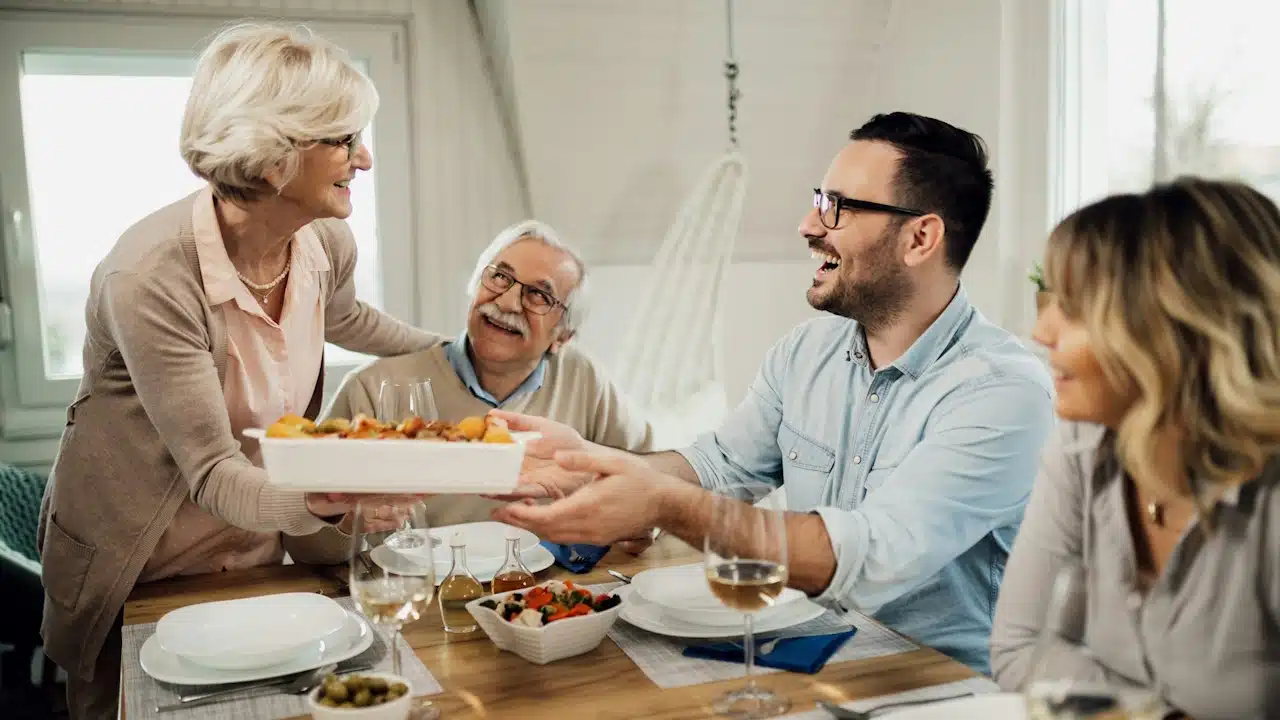 Happy senior talking to her adult son while bringing food at the dining table.