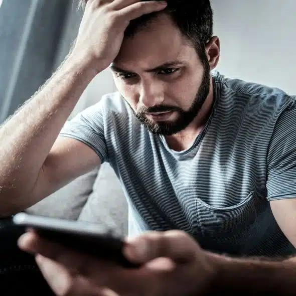 man sitting thoughtfully while looking at phone