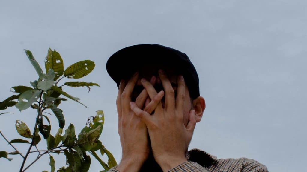 A person covering their face with both hands outdoors.