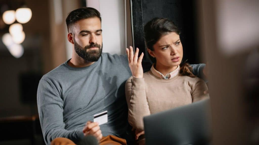 A woman gestures with frustration at a laptop while a man holds a credit card.