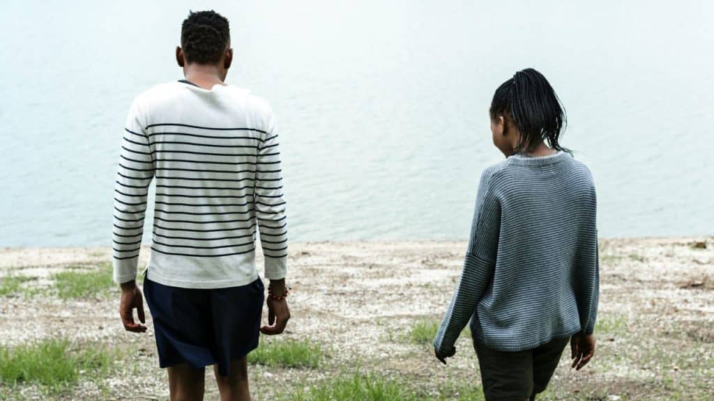 A man and woman stand on a dirt bank looking out at a body of water.