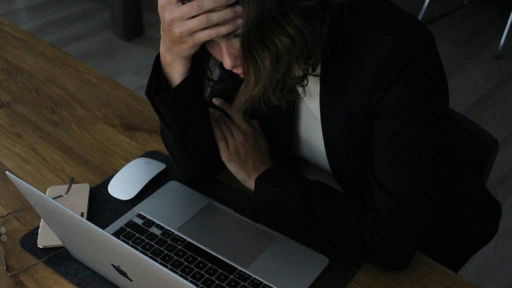 A person holding their head while looking stressed at a laptop on a desk.