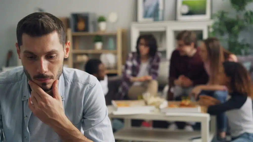 A man rests his chin on his hand while a group talks in the background.