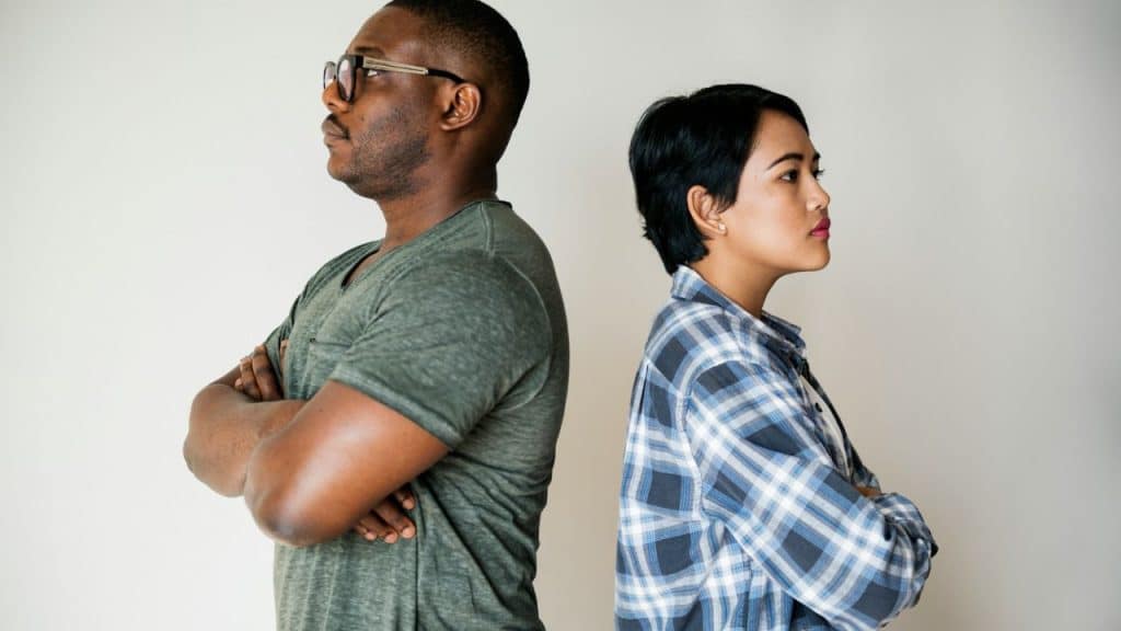 A man and woman standing back-to-back with their arms crossed against a white wall.
