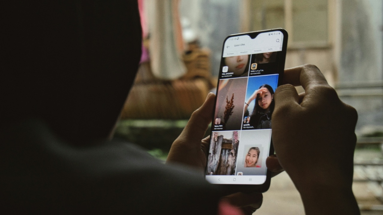 A person’s hands hold a smartphone displaying a grid of various profile pictures of women.