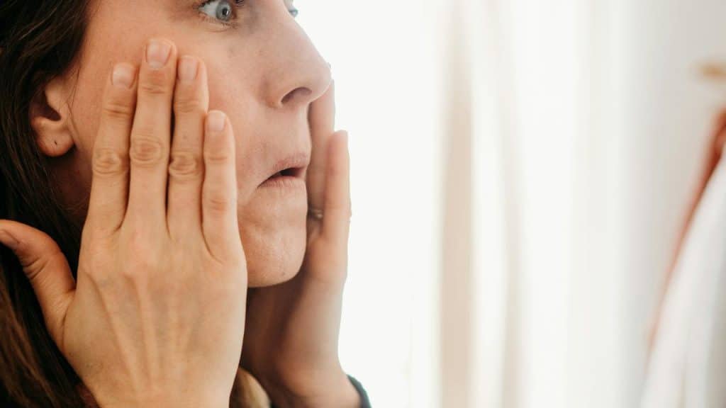 A woman holding her face while looking in a mirror.