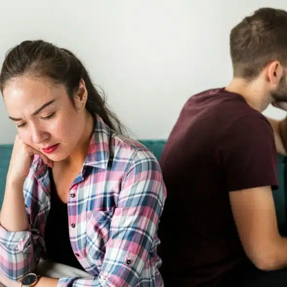A man and woman sit back-to-back on a teal sofa looking in opposite directions.