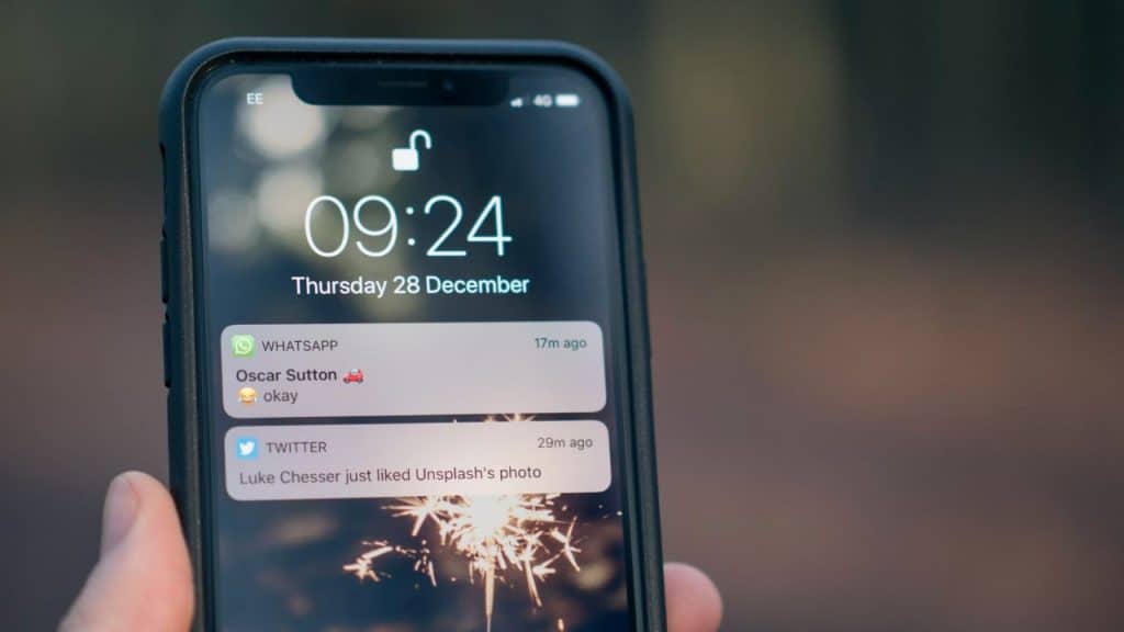 A hand holds a smartphone displaying notifications from WhatsApp and Twitter on the lock screen.