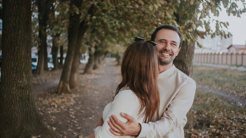 A smiling man hugging a woman on a tree-lined path.