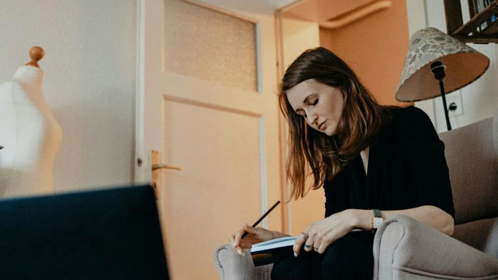 A woman sits in a chair writing in a notebook