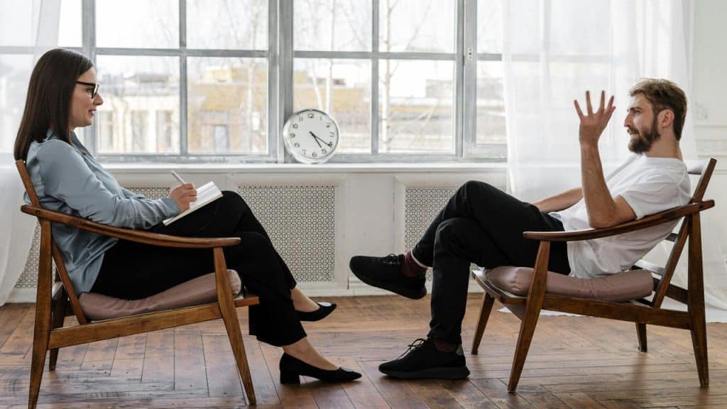 A therapist taking notes while a man speaks during a counseling session.