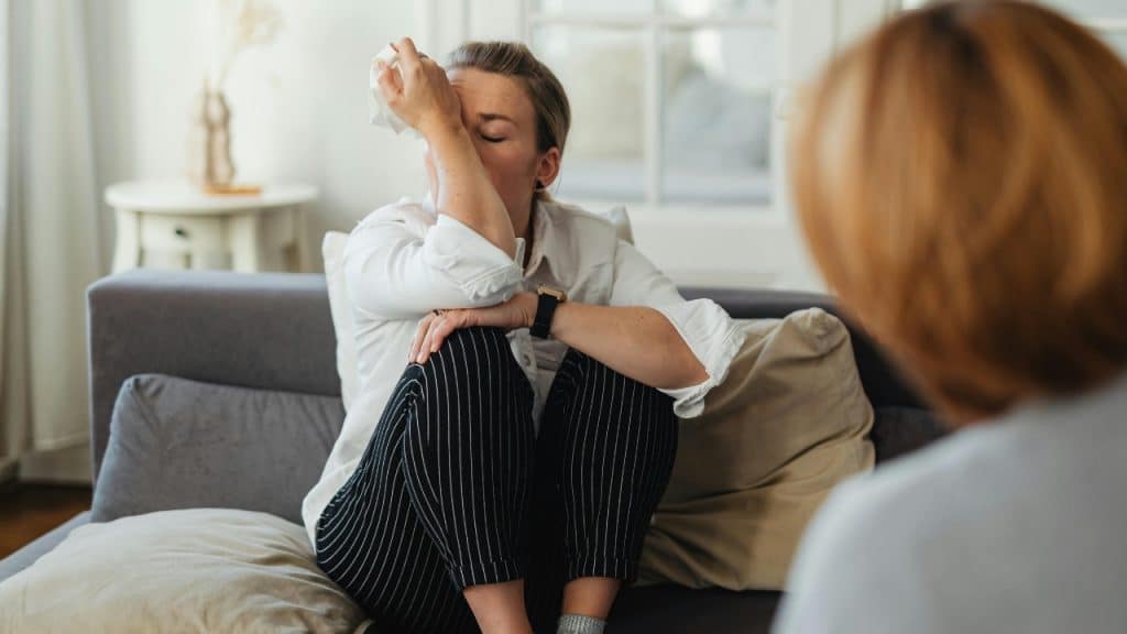 A woman in pinstriped pants sits on a sofa holding a tissue to her forehead.