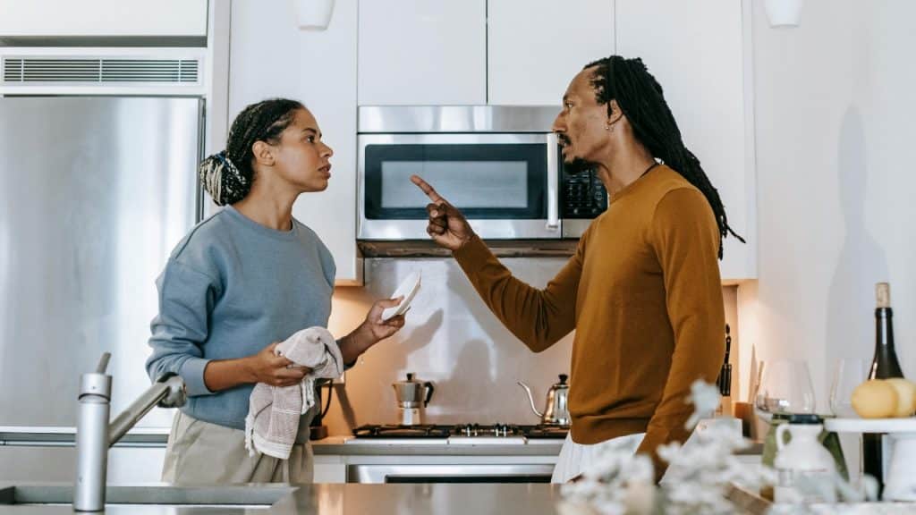 A man points a finger at a woman holding a towel in a modern kitchen setting.