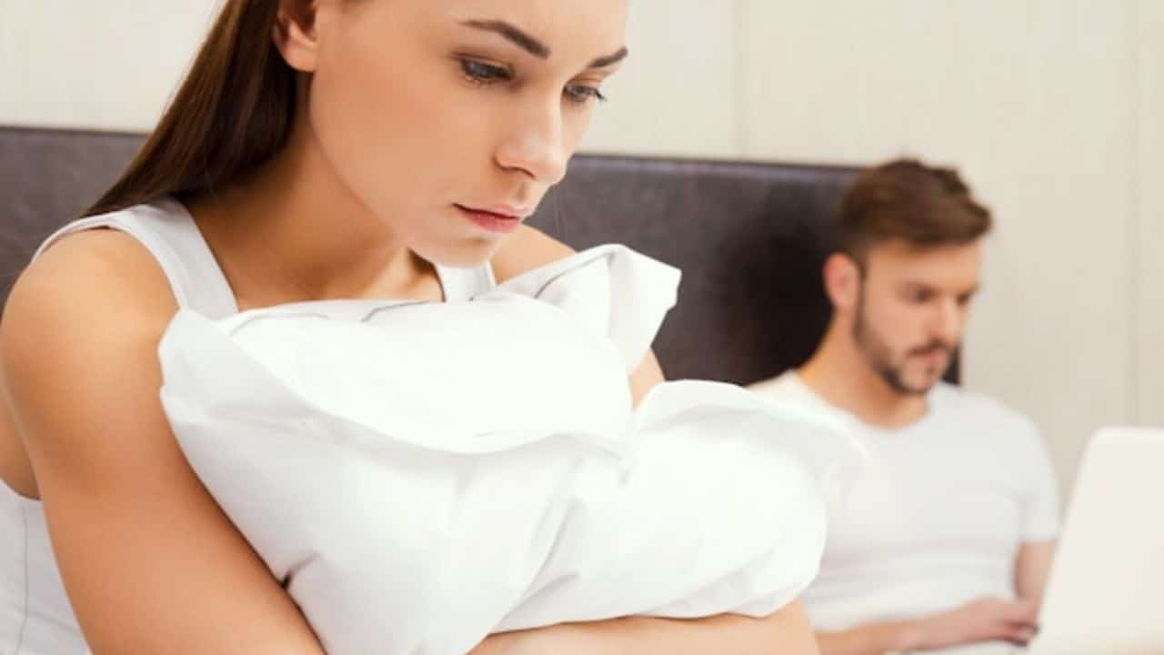 A woman clutches a white pillow while a man works on a laptop behind her.