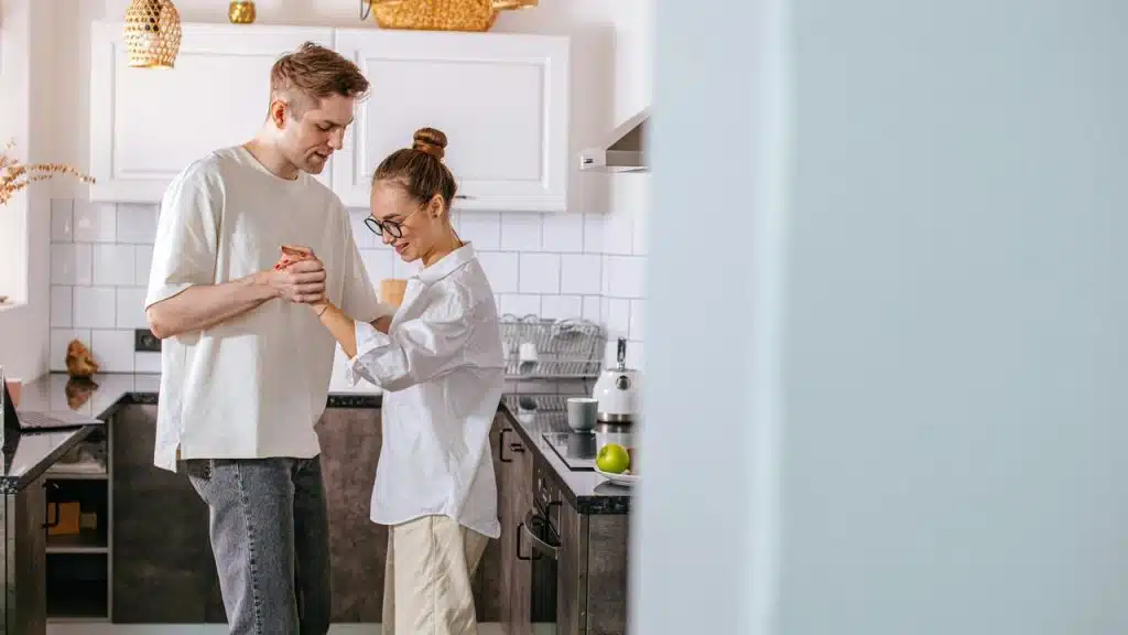 A couple holding hands and smiling together in a kitchen.