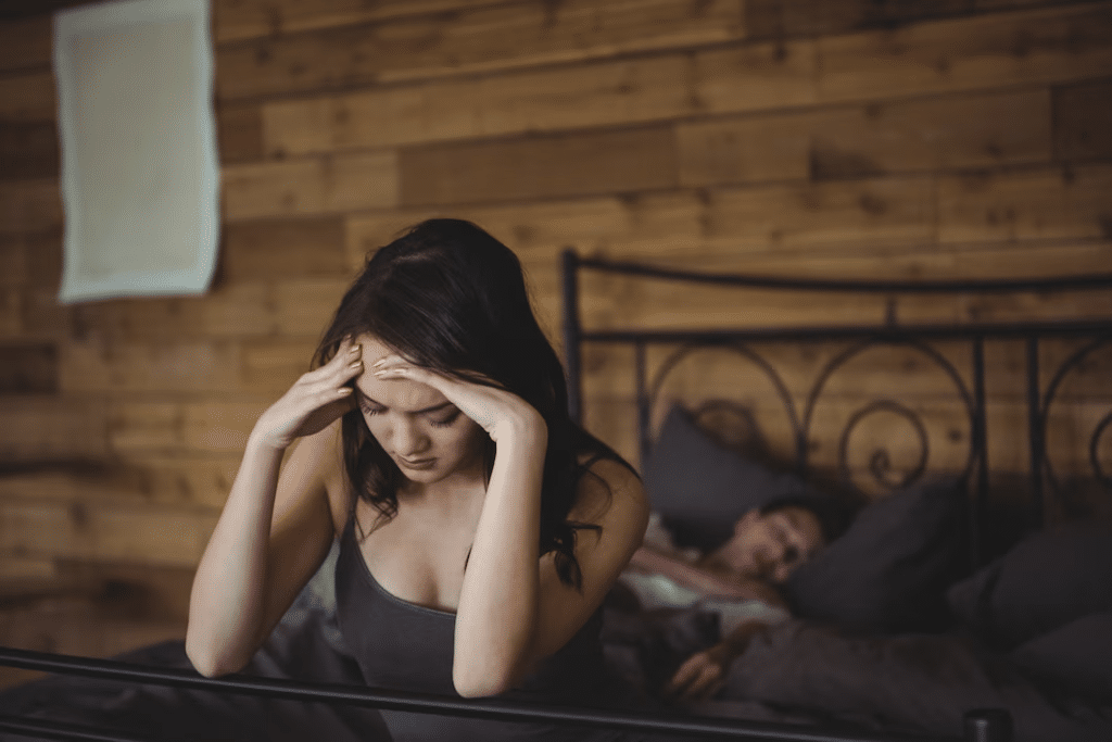 Upset woman sitting on a bed while man sleeping in background