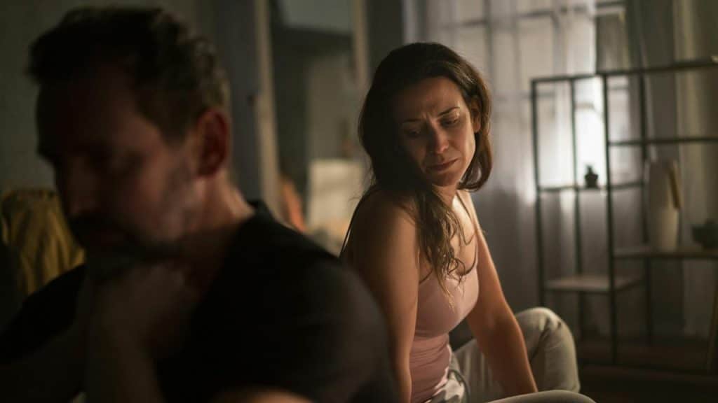 An upset mature man with his wife in bed behind him, The couple having relationship problems.