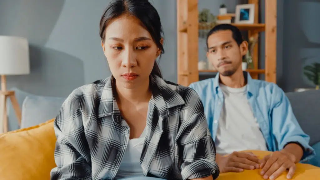 Upset asian couple sitting on couch in living room