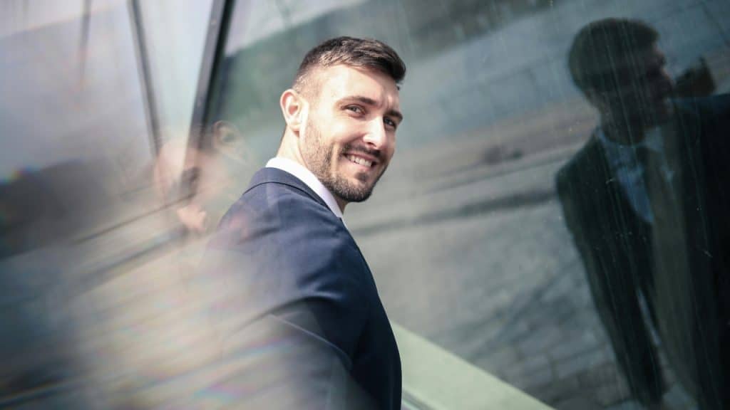 A man in a blue suit smiles and looks over his shoulder toward the camera lens.