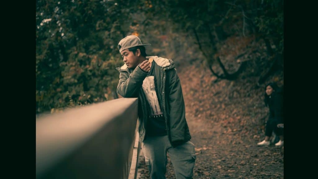 A man leaning on a rail next to a forest.
