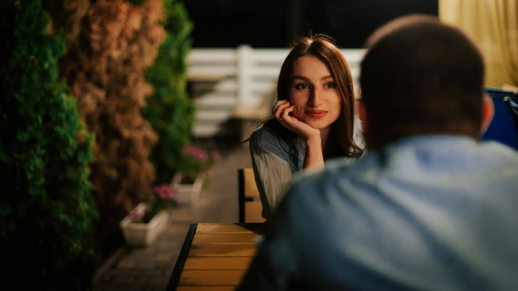 A woman rests her chin on her hand, looking at someone across a table.