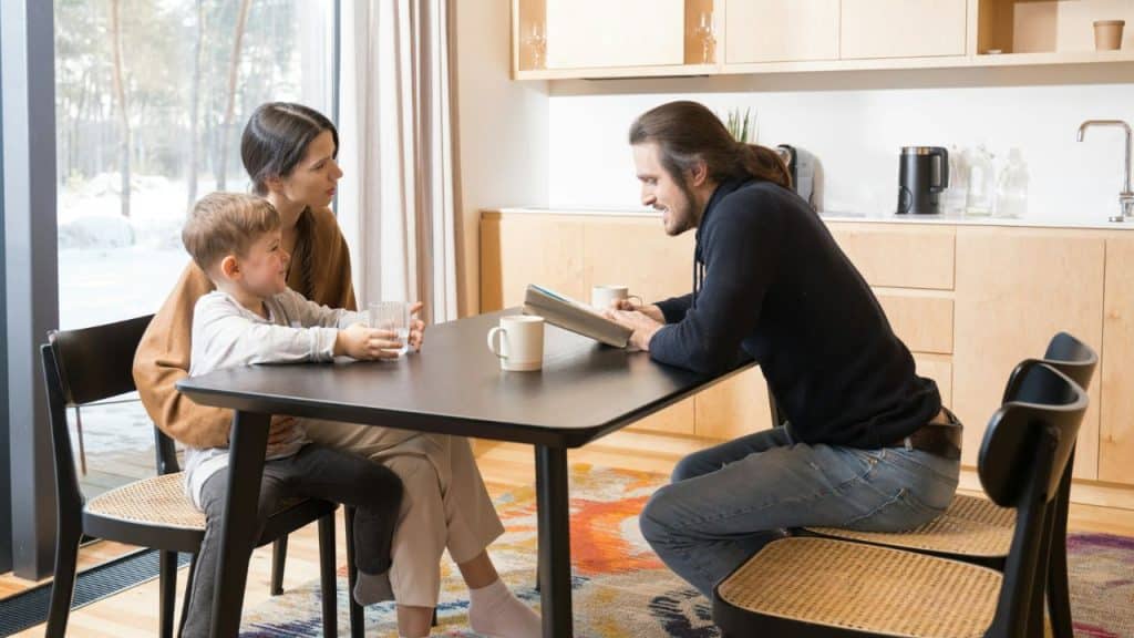 A man and woman sit at a kitchen table with a young boy between them.