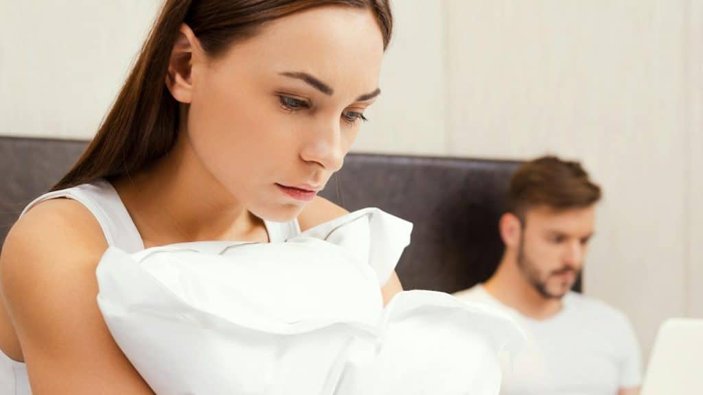 A woman looking sad while a man works on his laptop in the background. 