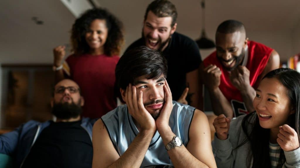 A man sits with his hands on his face while others celebrate around him.