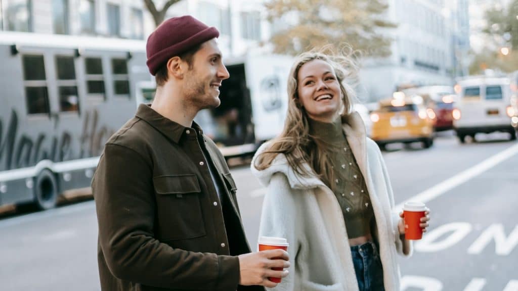 A man and woman walk down a city street holding paper coffee cups.