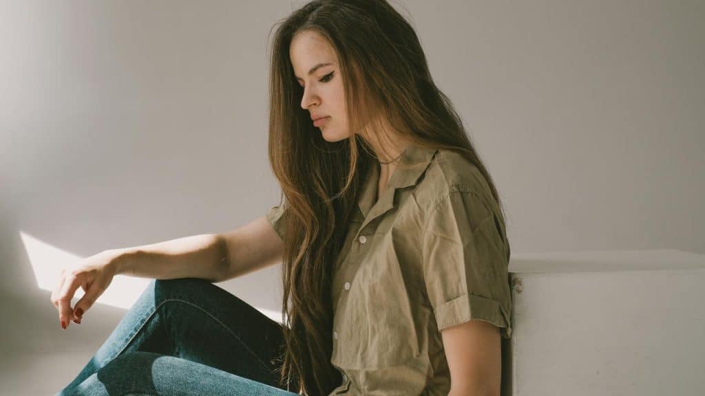 A woman sitting quietly and looking down in soft sunlight.