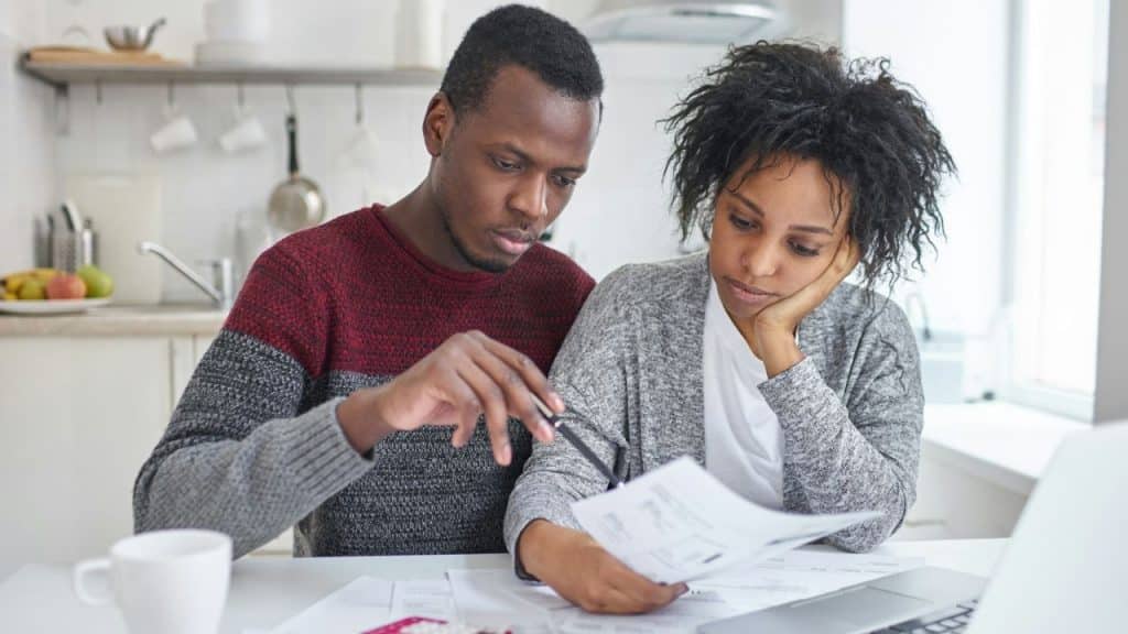 A man points a pen at paperwork while a woman rests her head on her hand.