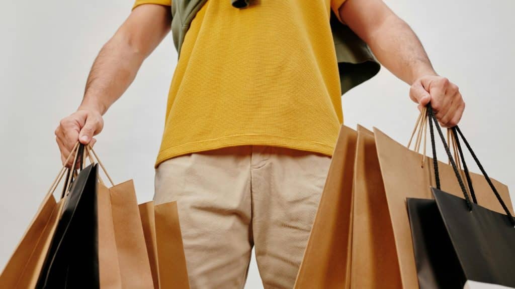 A person in a yellow shirt holds several brown paper shopping bags in both hands.