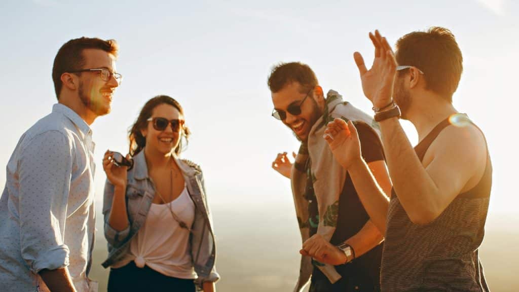 Four young adults laugh and talk together outdoors under a bright, sunny sky.
