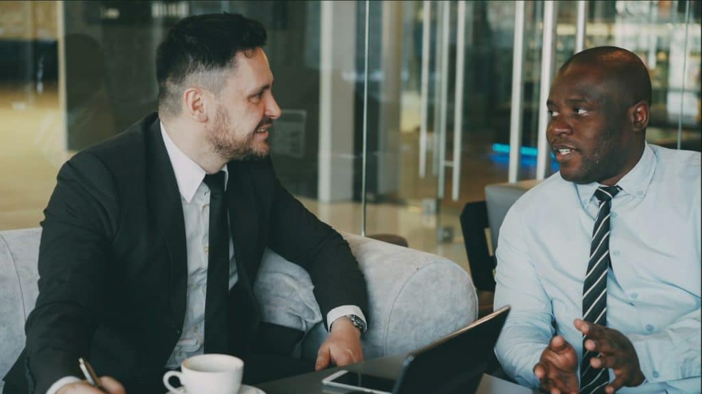 Two men in business attire are sitting and talking in a modern office space.