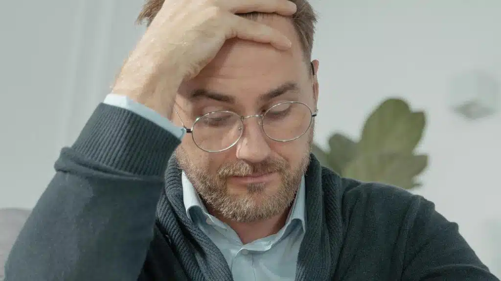 A man wearing glasses holding his head while looking down.