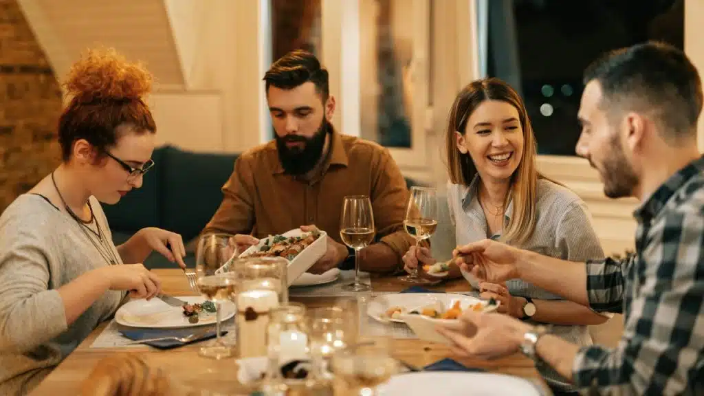 Four people sit around a dining table eating a meal with wine glasses and lit candles.