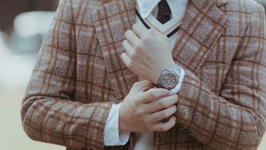 A person in a plaid blazer and white sweater adjusts their silver wristwatch.