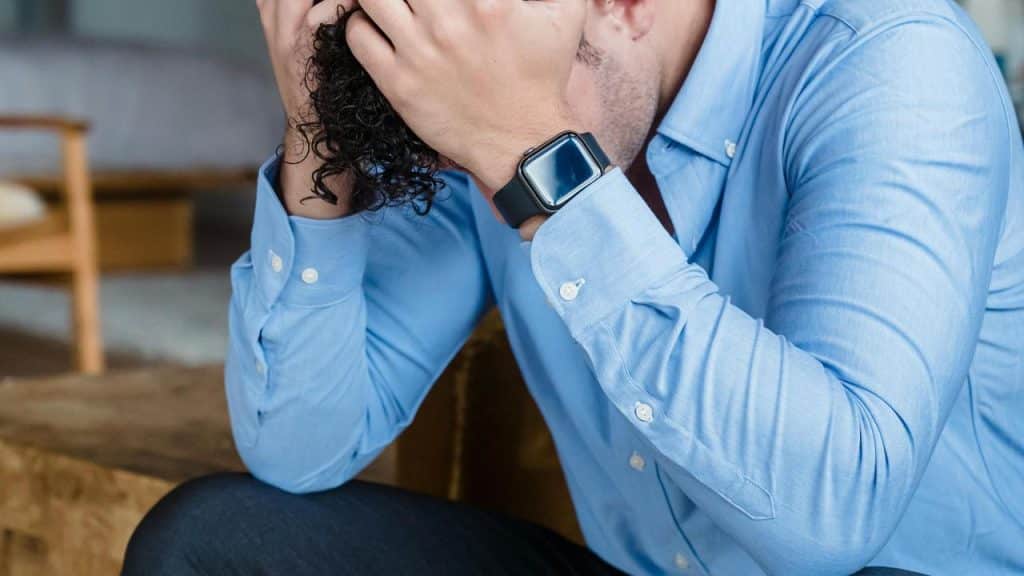 A man holding his head in stress while sitting down.