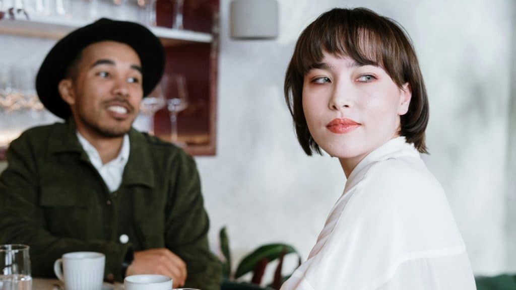 A woman looks away while a man in a hat sits behind her.