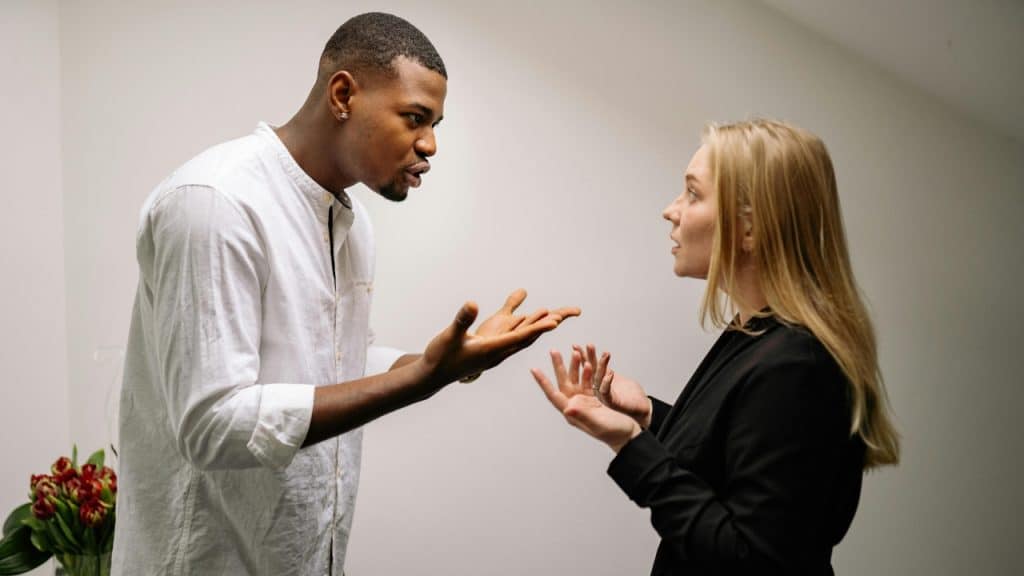 A man and woman stand facing each other, gesturing while having an intense conversation.
