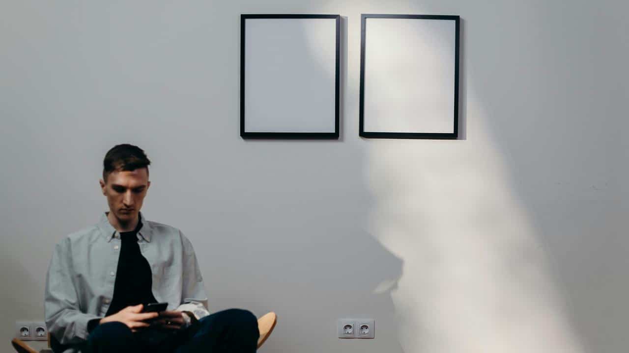 A man sitting in a minimalist room using a smartphone