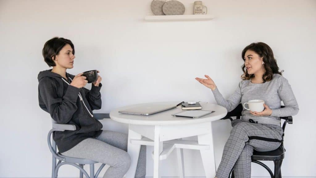 A woman talking while another woman listens over coffee at a table.