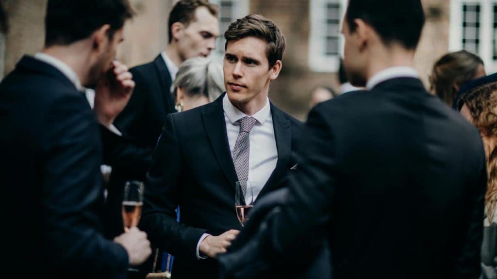 A group of men in suits standing together at a formal event, holding drinks and talking.